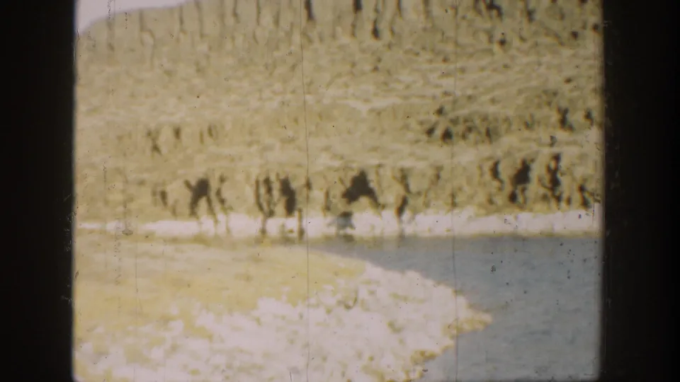 Faded 1936 California 8mm frame showing shoreline rocks, still water, and a hillside across the water.