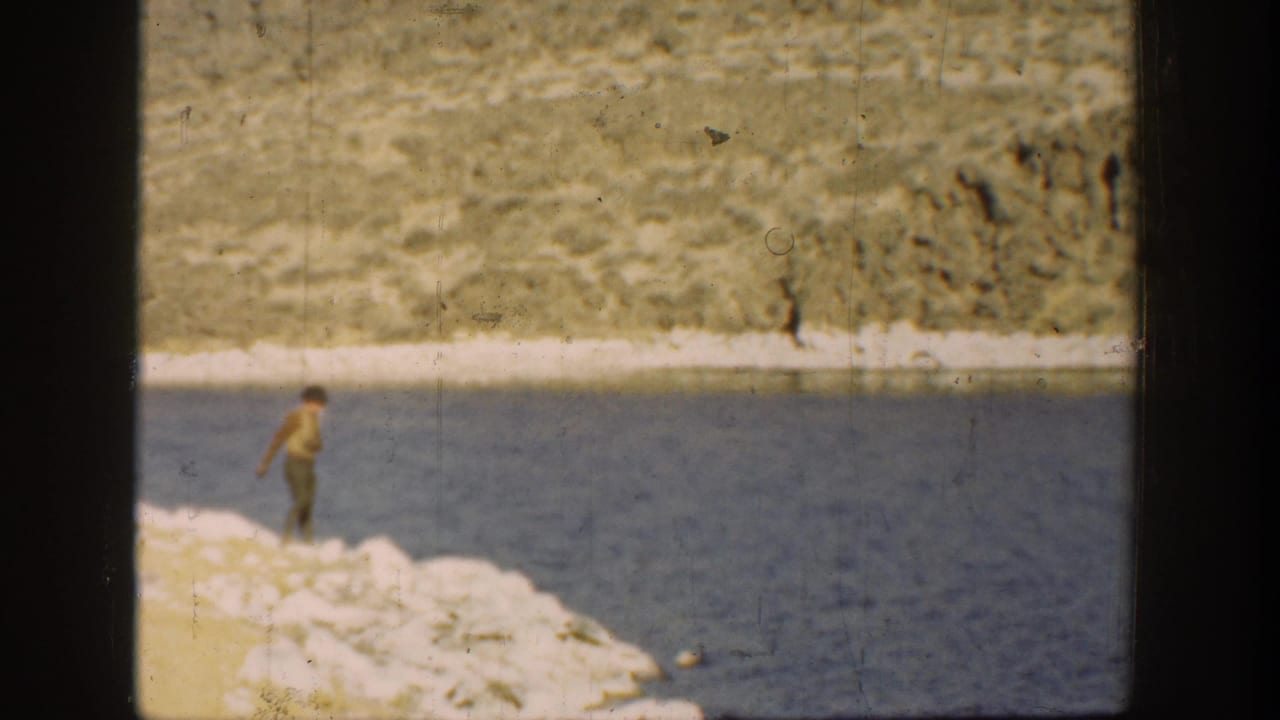 1936 California 8mm frame showing a distant man on a pale rocky riverbank beside blue water and dry slopes.
