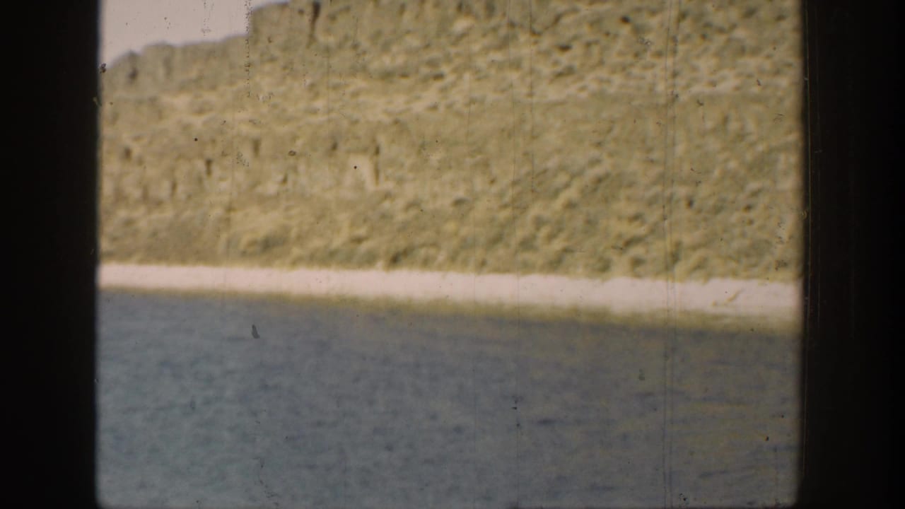 1936 California riverside view with still water, a pale bank, and rugged hillside behind dark frame bars.
