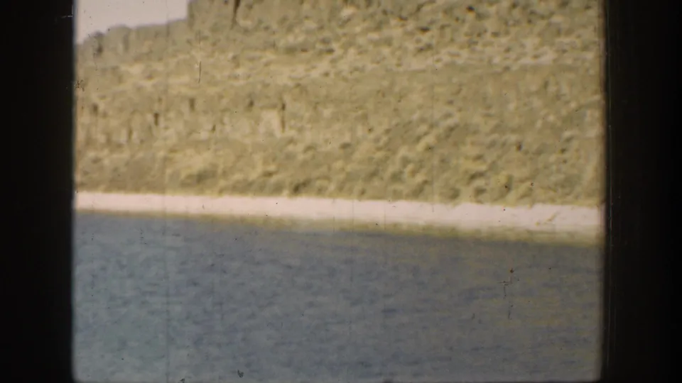 A 1936 California 8mm view of water, pale bank, and dry hillside framed by dark vertical and horizontal edges.