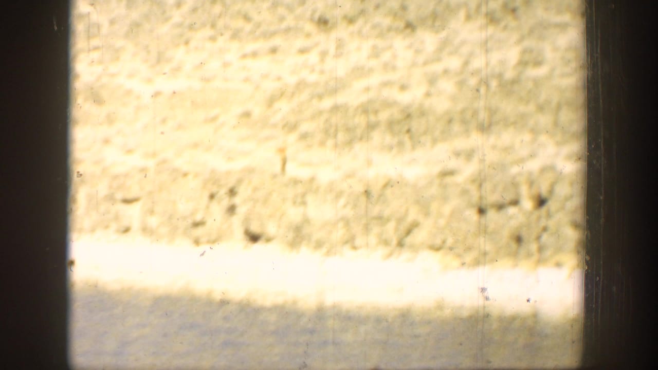 1936 California home-movie frame showing water, sunlit shoreline, rocky terrain, and visible 8mm gate edges.