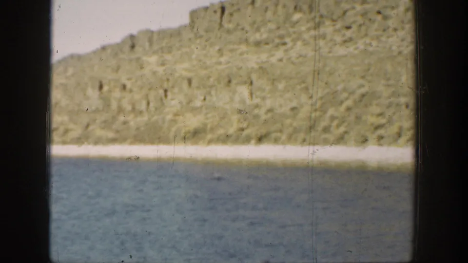 1936 California 8mm still of calm water below a rocky shoreline, framed by dark home-movie gate edges.