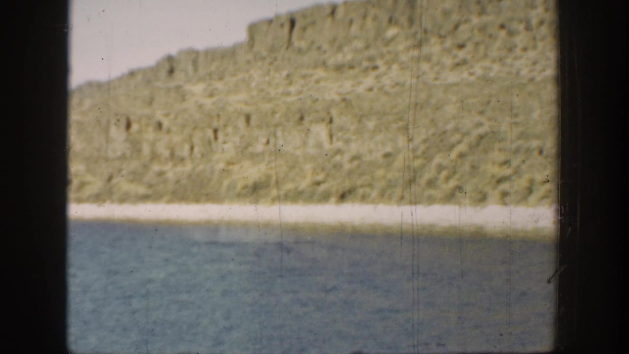 1936 California 8mm frame showing lagoon water, a light shore strip, and rocky cliffs under a bright sky.
