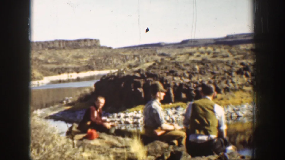 1936 California 8mm frame showing three men relaxing beside lagoon rocks, with water and rugged cliffs in the background.