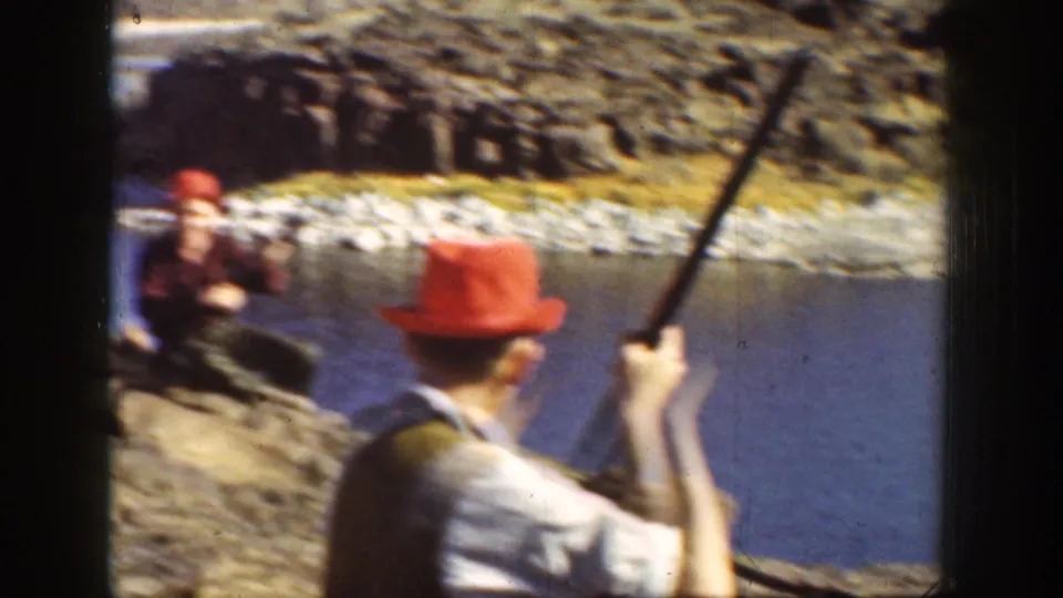 1936 California home-movie close view of men in red hats handling long guns on rocks beside a river.