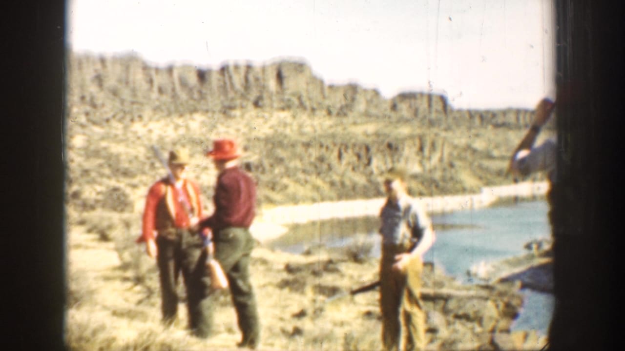 1936 California 8mm frame of four men in red hats and work clothes standing with long rifles in rugged open terrain.