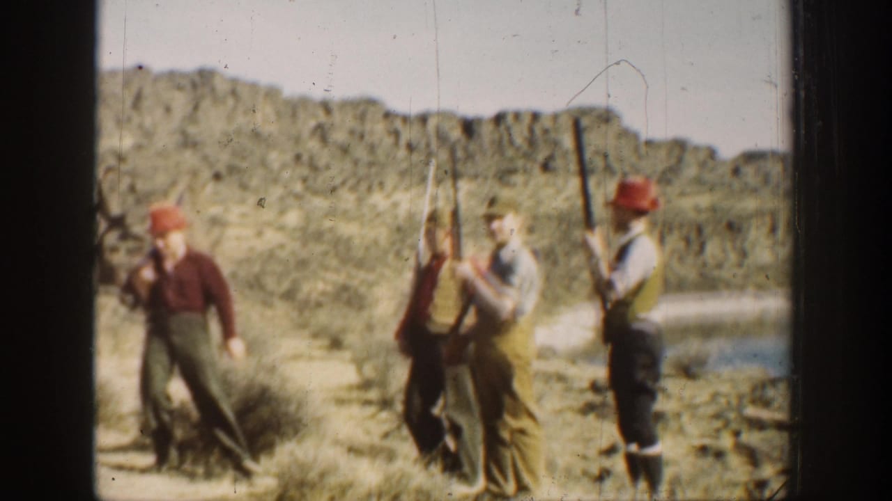 Men in period outdoor clothing hold long rifles upright against a rocky California desert backdrop in this 1936 home-movie frame.