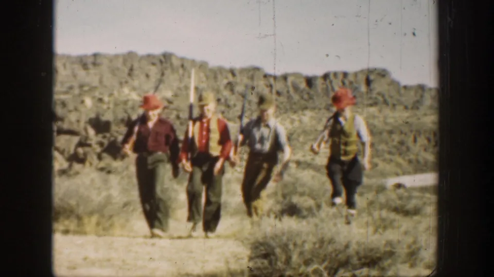 In metadata-supported 1936 California footage, four young men in hats and vests march across a desert landscape while carrying long rifles.