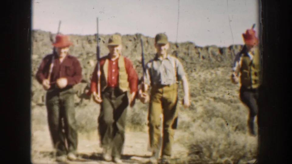 Three of the young men are close to camera in the desert, with rifles and period clothing visible as another figure exits at right.