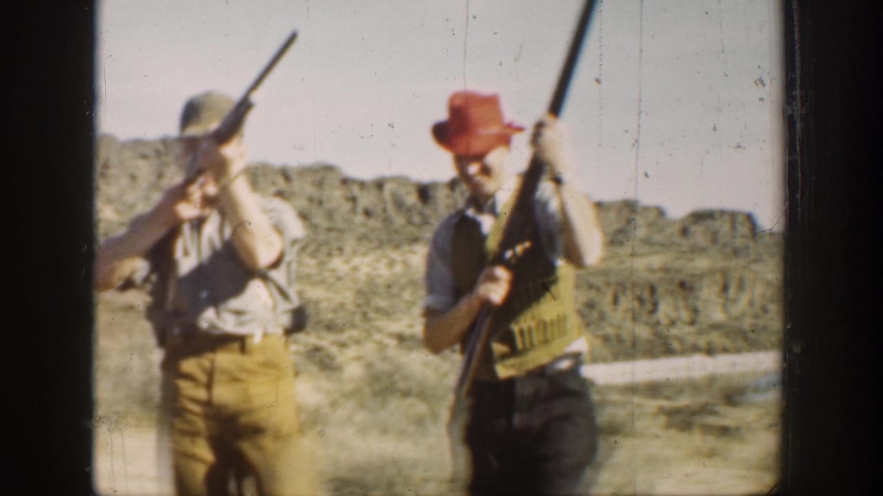 1936 California home-movie frame showing two men in hats and field clothing handling rifles in a dry open landscape.