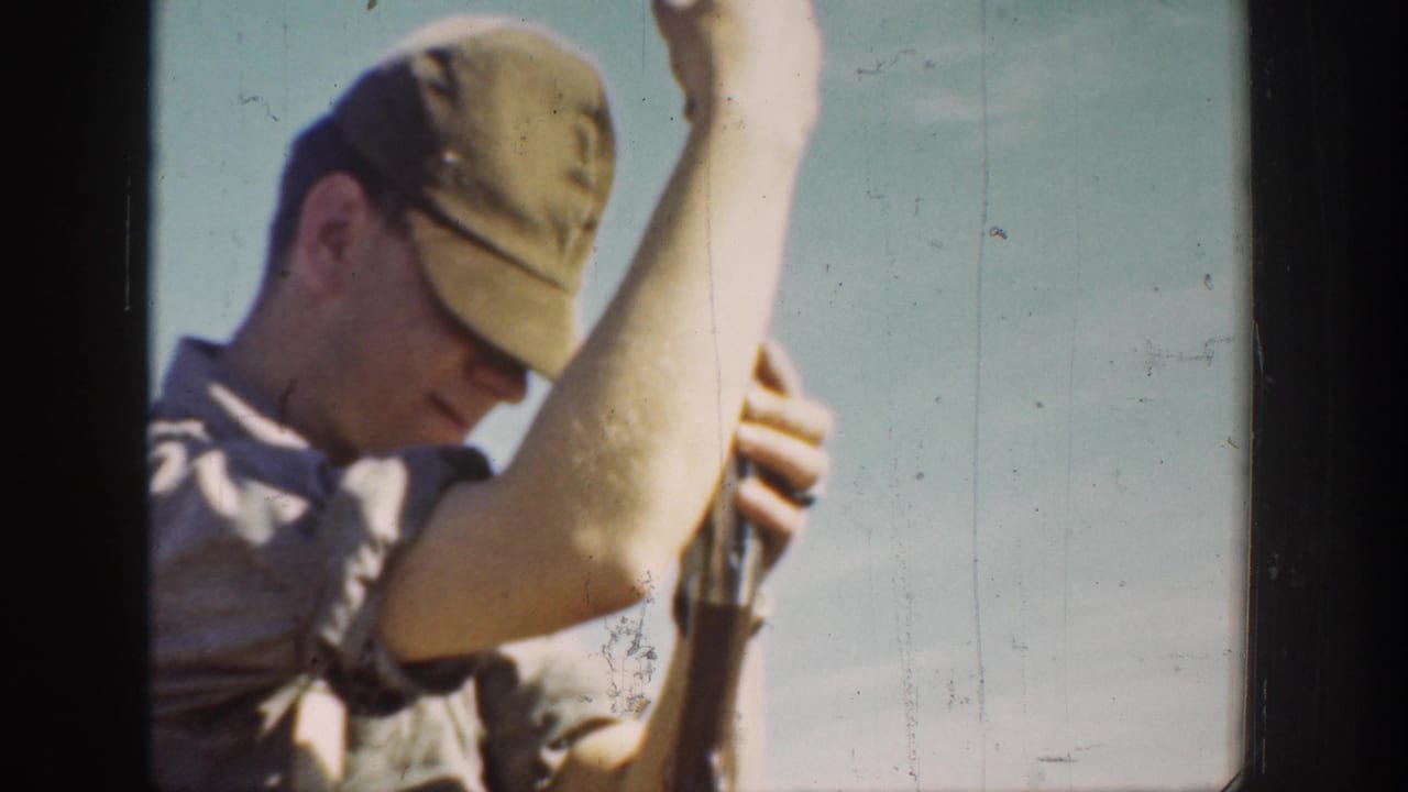 Close 1936 California frame of a man in a cap and rolled sleeves holding a rifle upright during outdoor practice.