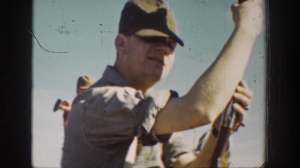 Close 1936 California home-movie frame with a man in a dark cap holding a rifle and other trainees partly visible behind him.