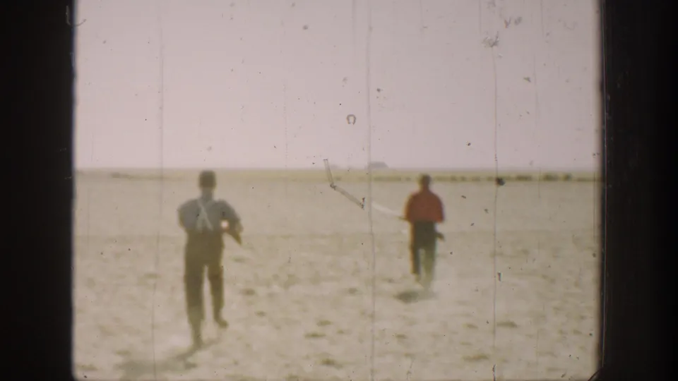 Wide 1936 California frame showing two figures moving across a sunlit dry field, with one appearing to carry a rifle.