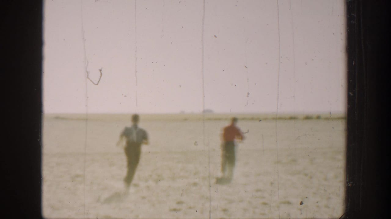 Two boys in 1930s California home-movie footage run away from the camera across a dry rural field.