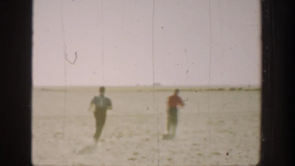 Two boys in 1930s California home-movie footage run away from the camera across a dry rural field.