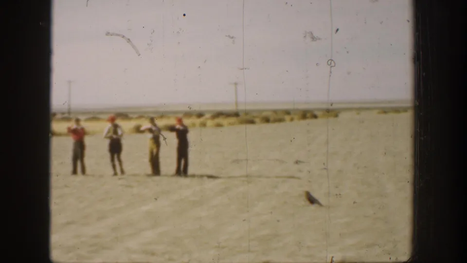 1936 California 8mm frame showing four men in a flat field, two appearing to raise long objects during hunting activity.