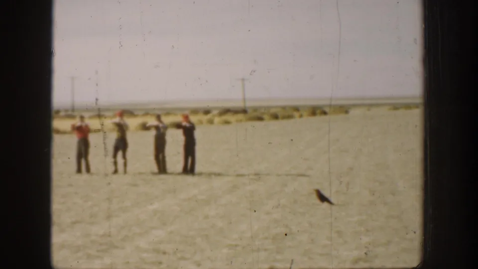 In 1930s California home-movie footage, four men stand in an arid field and aim rifles across the sand.
