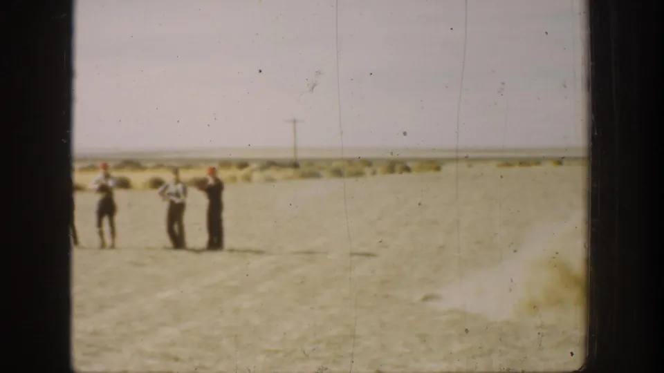 Three men remain in the open California field, appearing to handle or aim rifles in the distance.