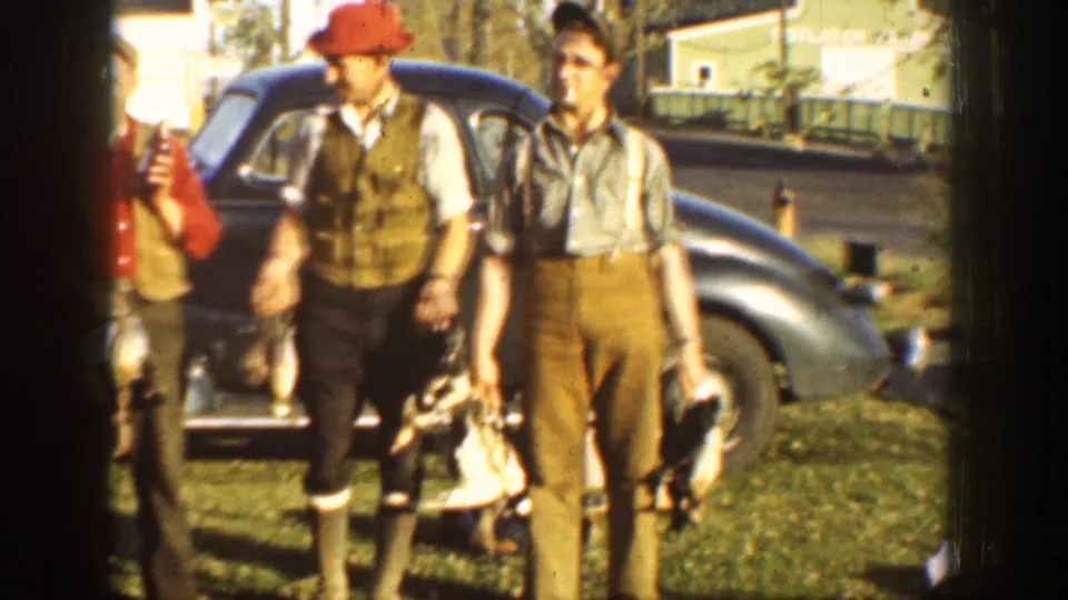 Men in 1930s-style outdoor clothing hold game birds beside a dark automobile in a California rural home-movie scene.