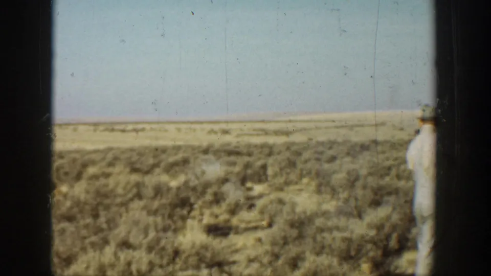 1936 California desert view with scrub, pale sky, dark frame bars, and a light-clothed man partly visible at the right edge.