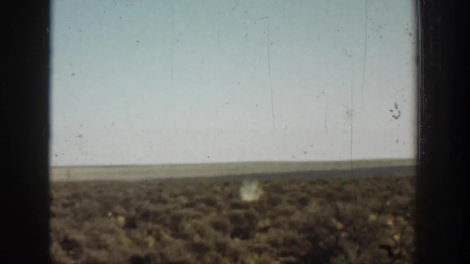 Faded 8mm view of an open California arid landscape, pale sky, and scrub-covered ground with no clearly identifiable structure.