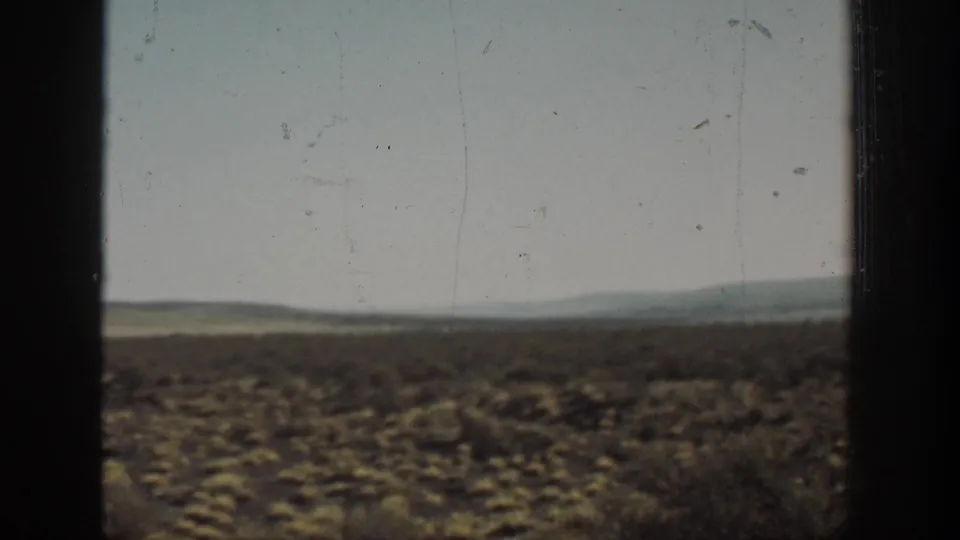 Wide 1936 California desert view with scattered shrubs, low hills on the horizon, faded color, and visible 8mm film wear.