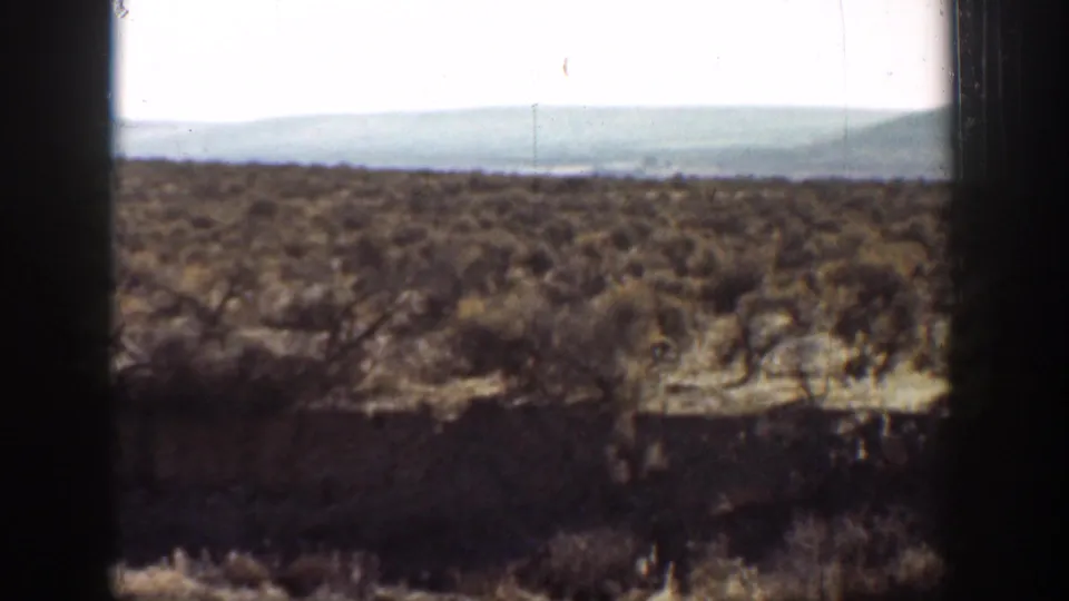 1936 California 8mm frame showing low scrubland, dark foreground shadow, distant hills, and a bright washed-out sky.