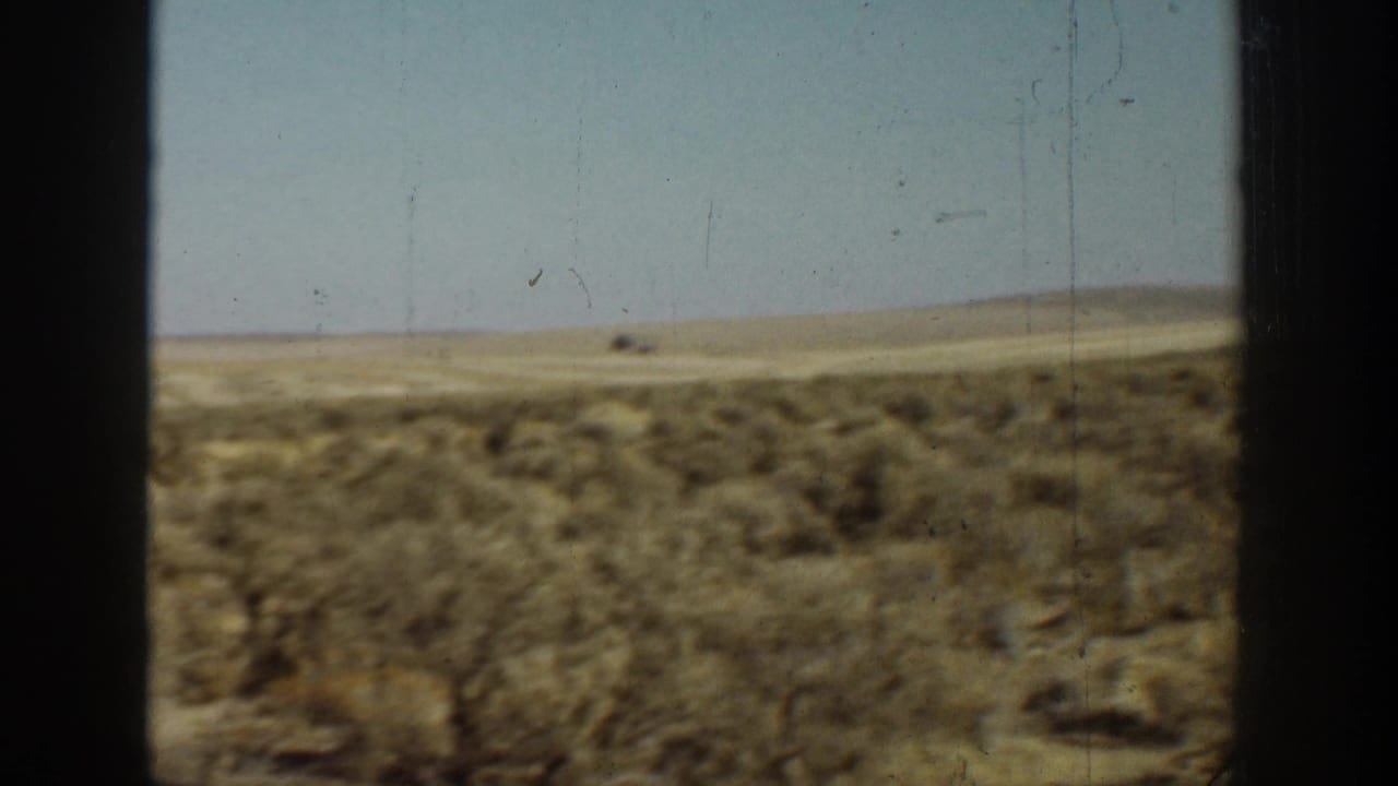 1936 California 8mm frame showing dry brush-covered desert ground, low hills, pale sky, and dark vertical window-like edges.