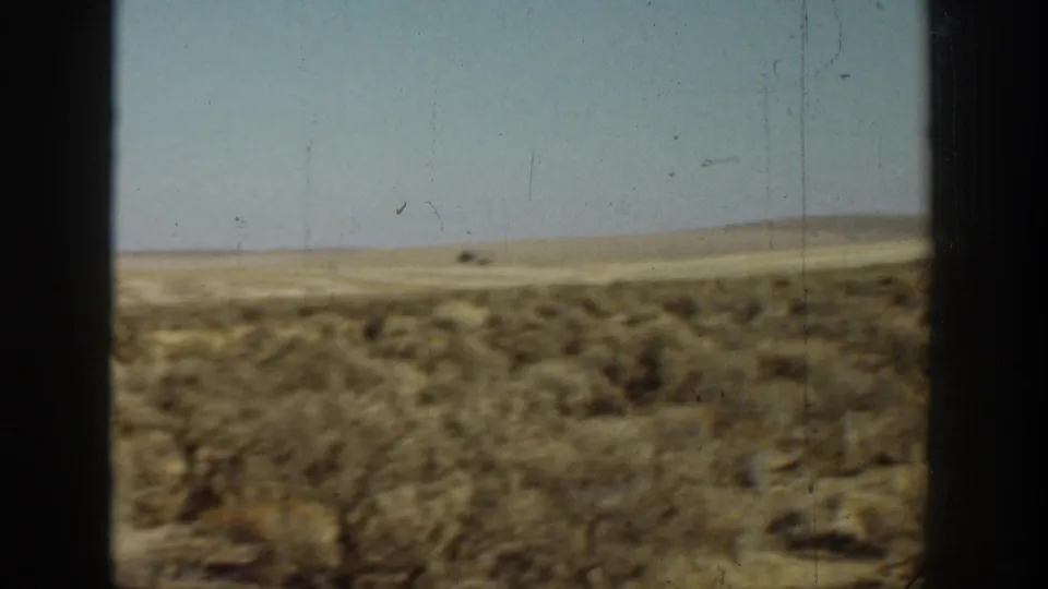 1936 California 8mm frame showing dry brush-covered desert ground, low hills, pale sky, and dark vertical window-like edges.