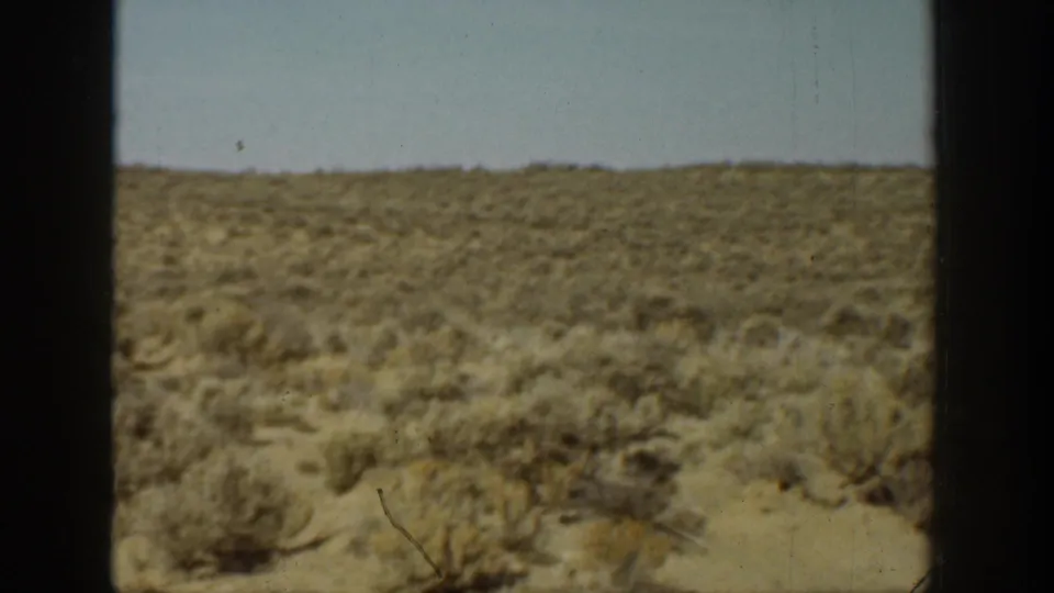 1936 California home-movie frame with arid brush, a low hillside, pale sky, and dark framing at the sides.