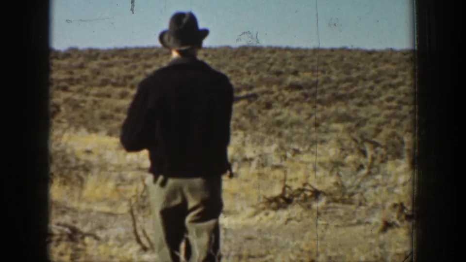 1936 California 8mm frame showing a man in a fedora and dark jacket walking away through dry desert brush.