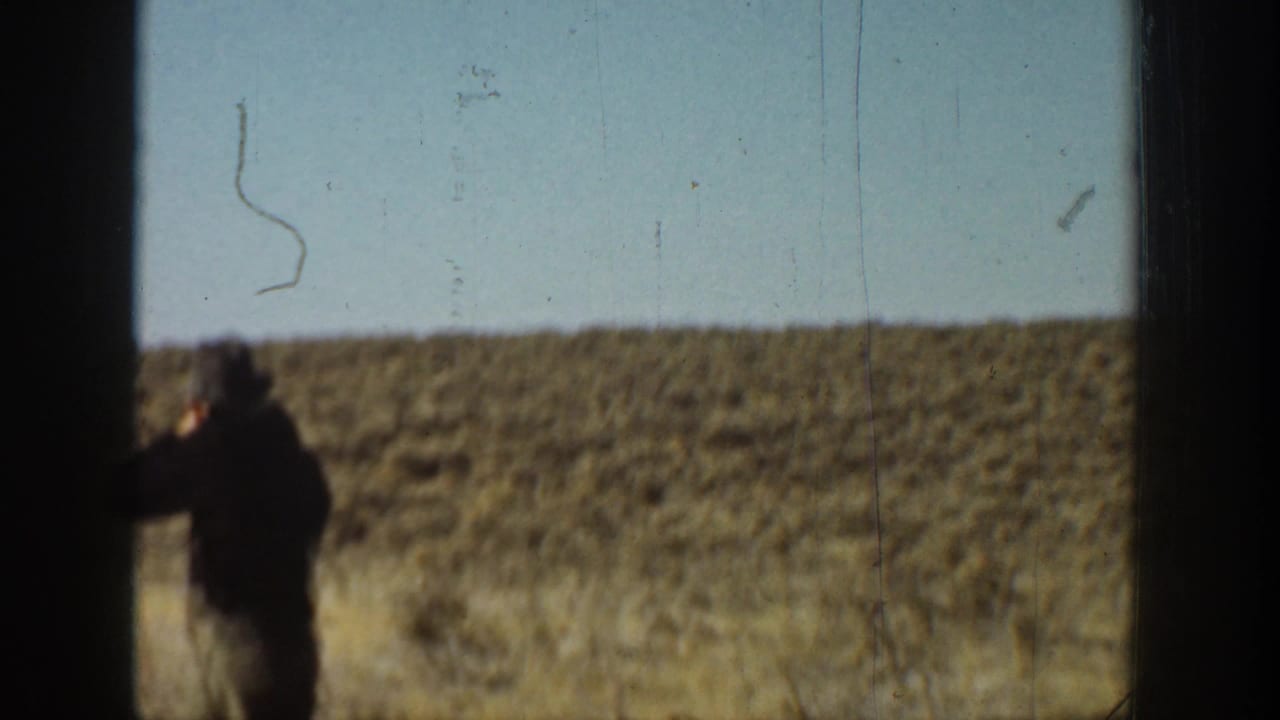 1936 California 8mm frame showing a hatted man from behind on a dry grassy hillside with shrubs and open sky.