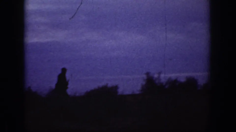 Dusk 8mm frame from the California hillside scene with a small silhouetted figure moving along low brush against a purple sky.