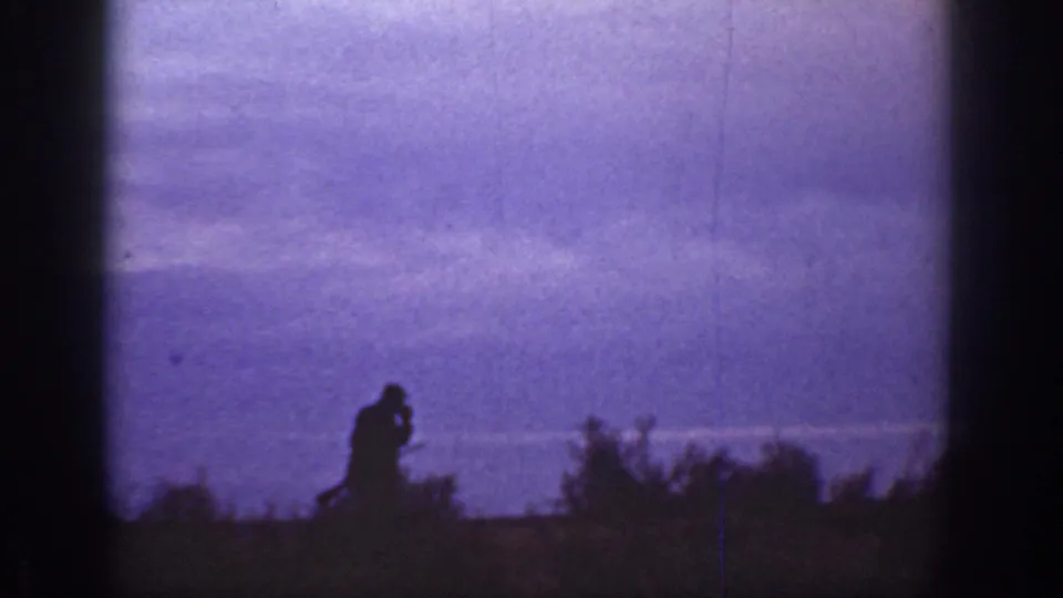 1936 California dusk frame showing the hatted man in silhouette near brush, hand near his face beneath a purple twilight sky.