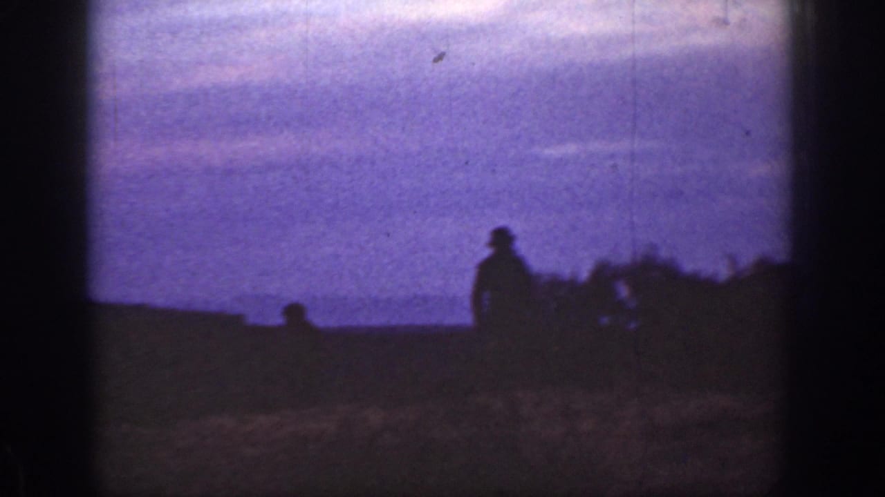 1936 California 8mm frame showing a dark human silhouette near low brush against a purple dusk sky.
