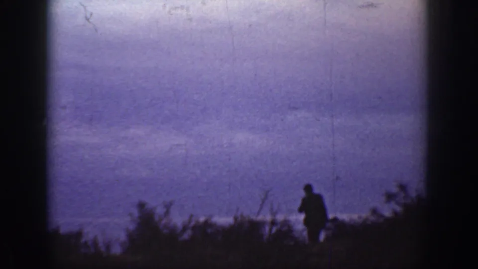 A 1936 California home-movie frame shows a human silhouette near scrubby vegetation against a low purple evening sky.