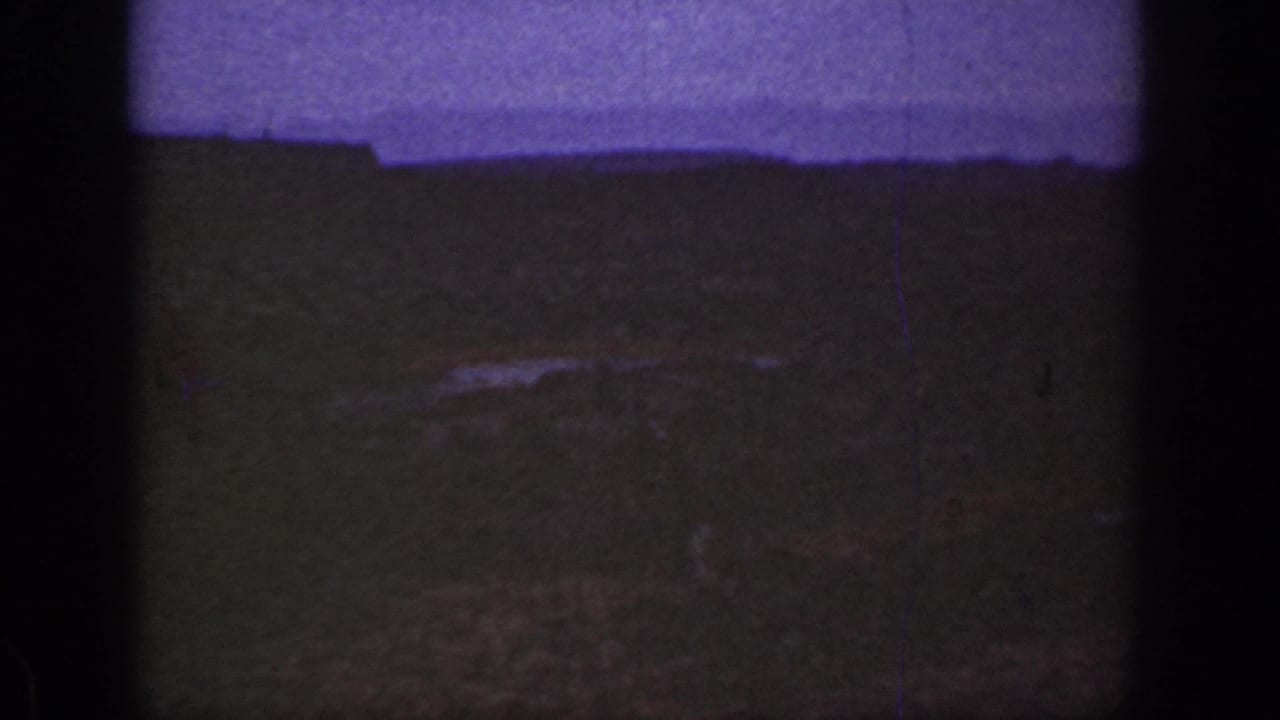 1930s California 8mm frame showing a dim semi-desert landscape, purple-tinted sky, and dark film gate edges.