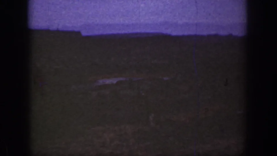 1930s California 8mm frame showing a dim semi-desert landscape, purple-tinted sky, and dark film gate edges.