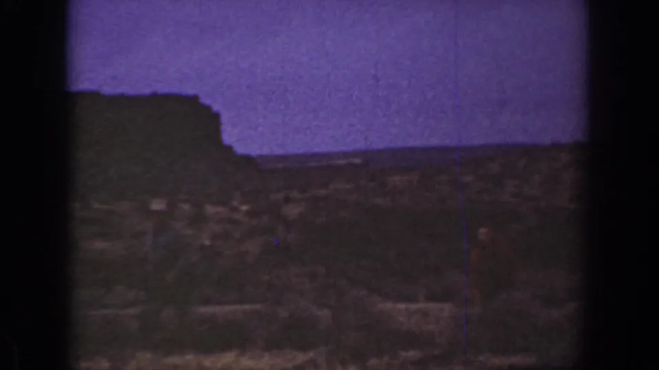 1936 California 8mm frame showing rough arid ground, low vegetation, a dark ridge, and a purple-tinted sky with no clear people visible.