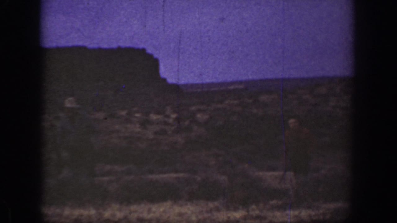 Arid ground and dark ridge with a faint adult figure near the center of the frame.