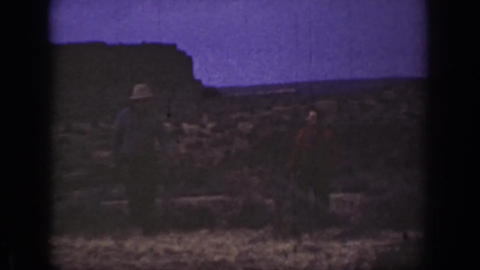 1936 California 8mm frame showing two adult men in dark clothing on rocky arid terrain, with one wearing a light-colored hat.