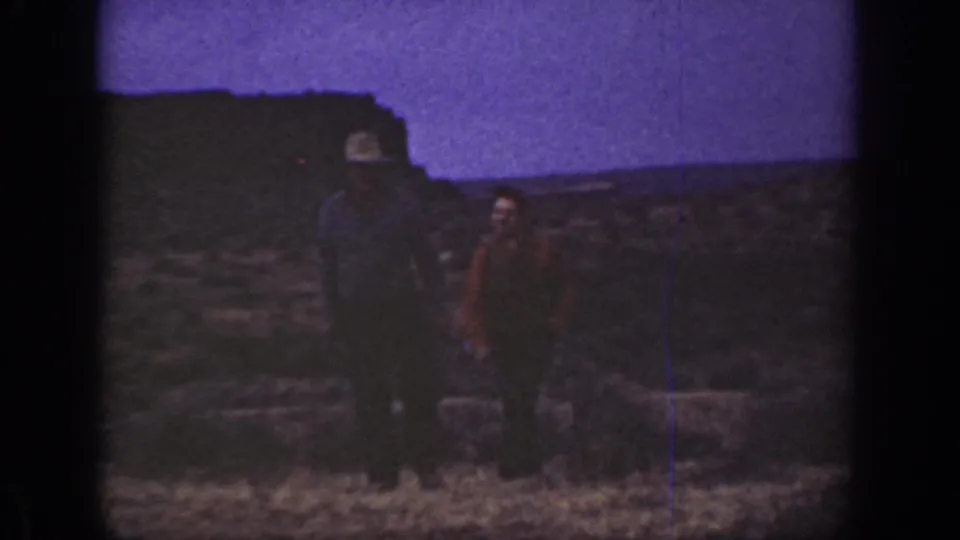 1936 California 8mm frame showing two adult men closer in view, one in a light hat, standing in a rocky arid landscape.