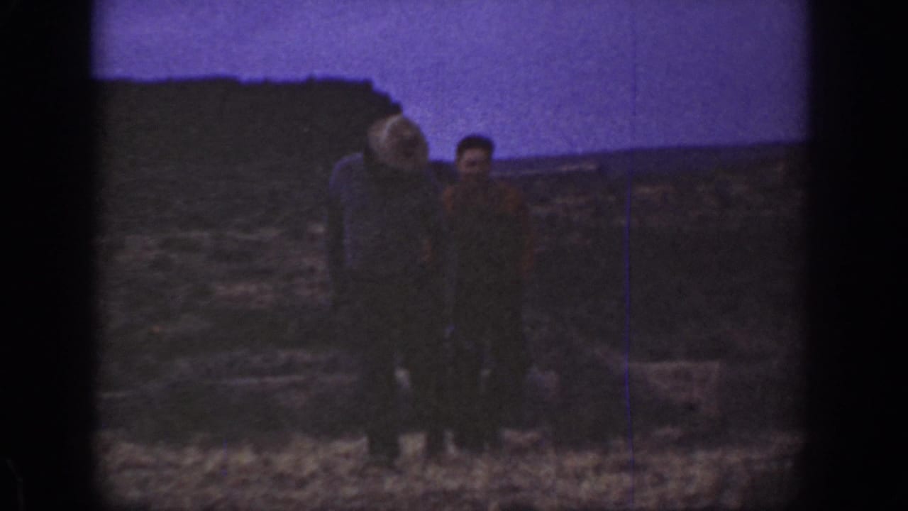1936 California home-movie frame showing two adult men walking through dry scrubland with low hills in the background.
