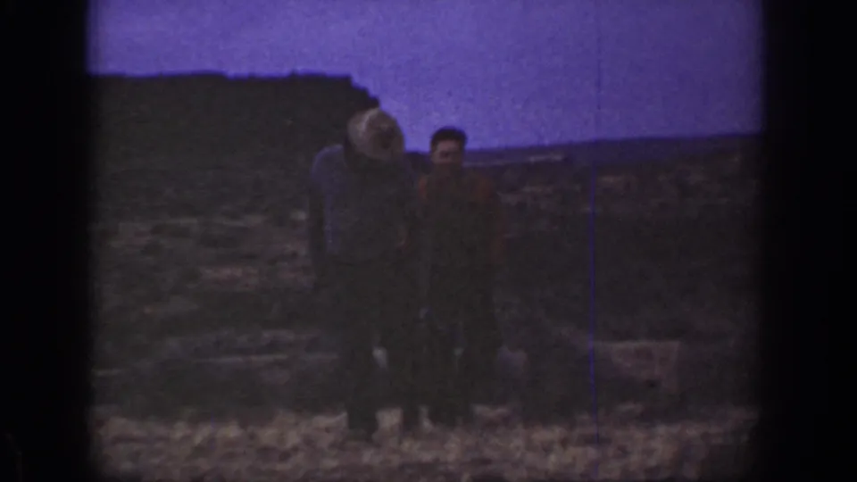 1936 California home-movie frame showing two adult men walking through dry scrubland with low hills in the background.