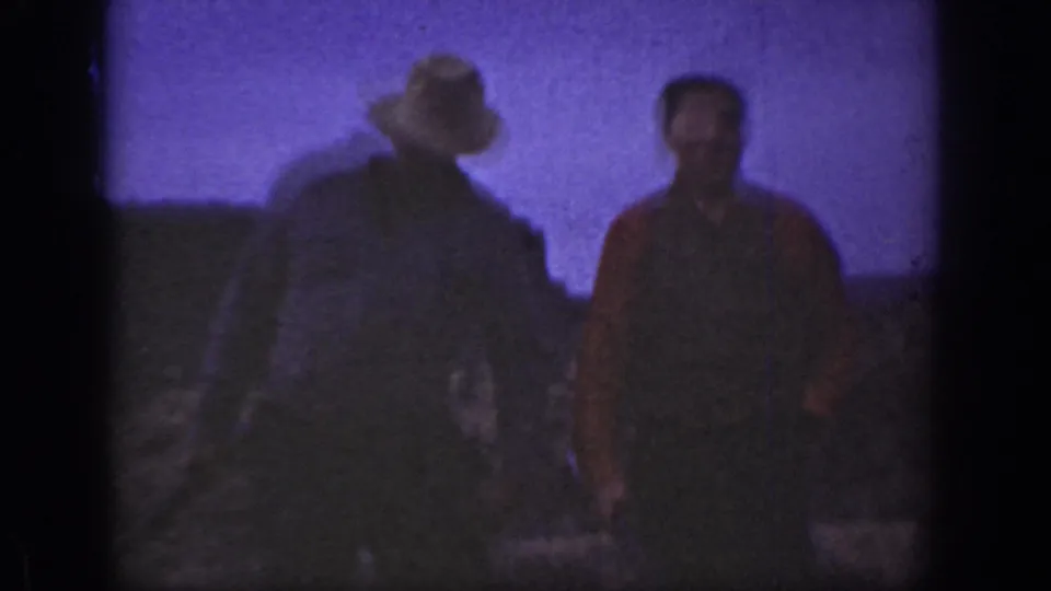 Close 8mm frame of two adult men in the California scrubland, one in a light hat and the other in a red shirt.