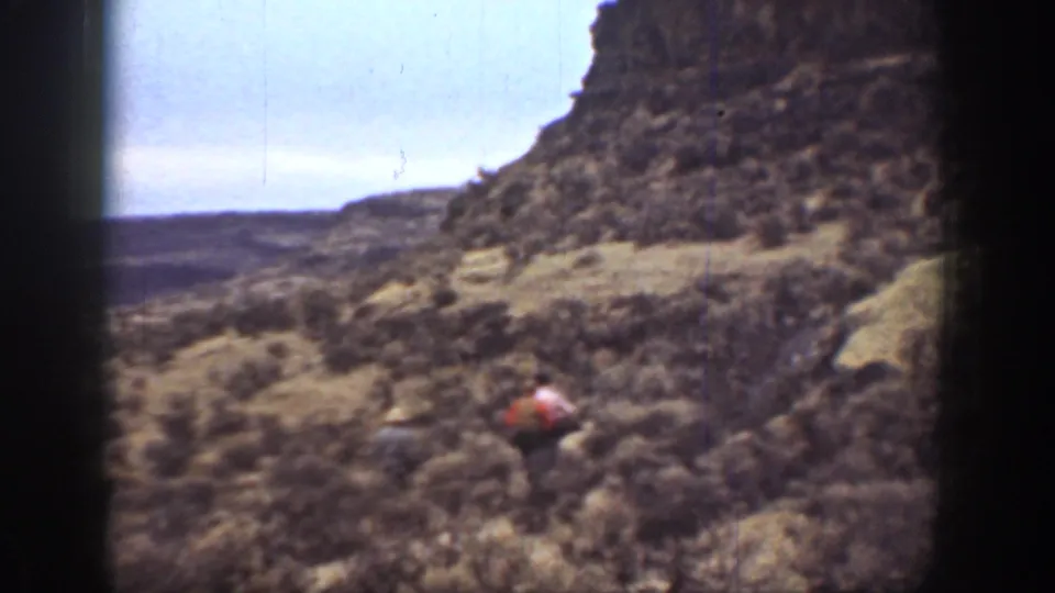Wide 1936 California landscape frame with rocky scrub hills and a small red-clad figure low in the terrain.