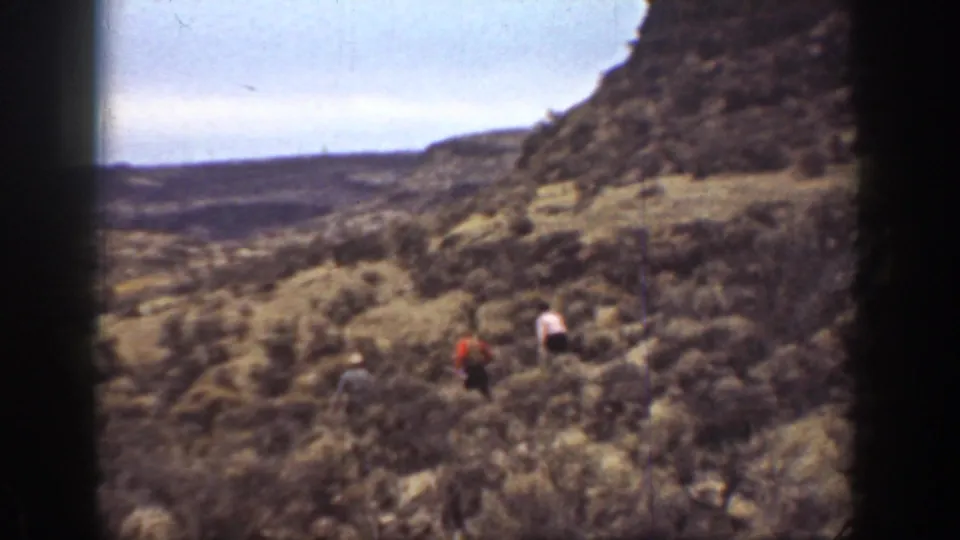 Distant hikers in 1936 California move across a brushy canyon slope, partly obscured by soft focus and film-frame shadows.