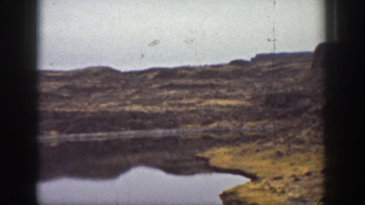 1936 California 8mm view of a still lake or reservoir set below dark rocky plateau slopes.