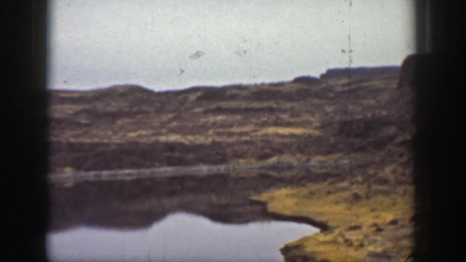 1936 California 8mm view of a still lake or reservoir set below dark rocky plateau slopes.
