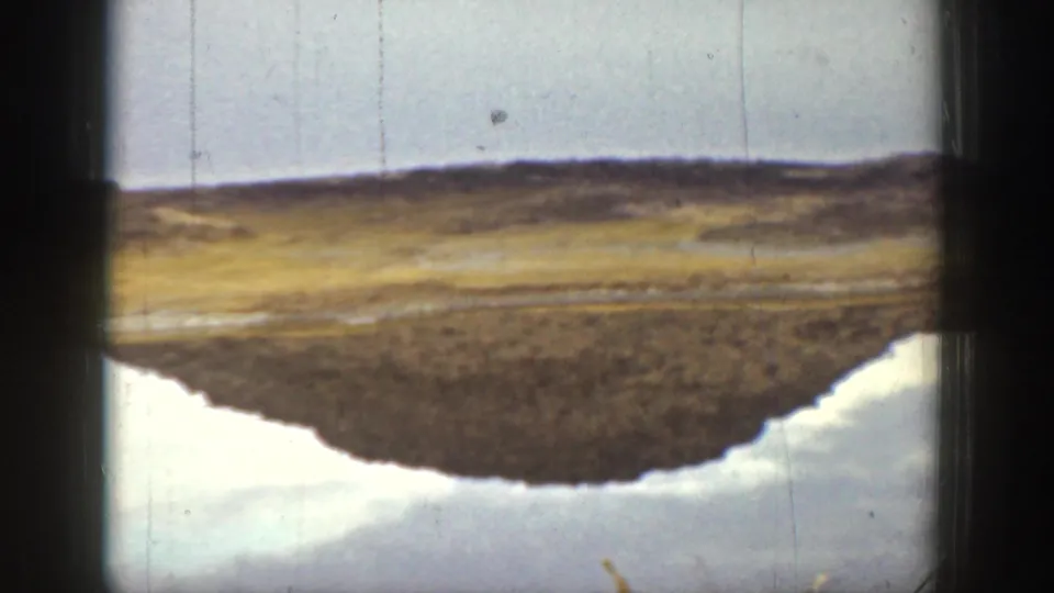 1936 California 8mm frame with calm water reflecting a low desert hill and open shoreline.